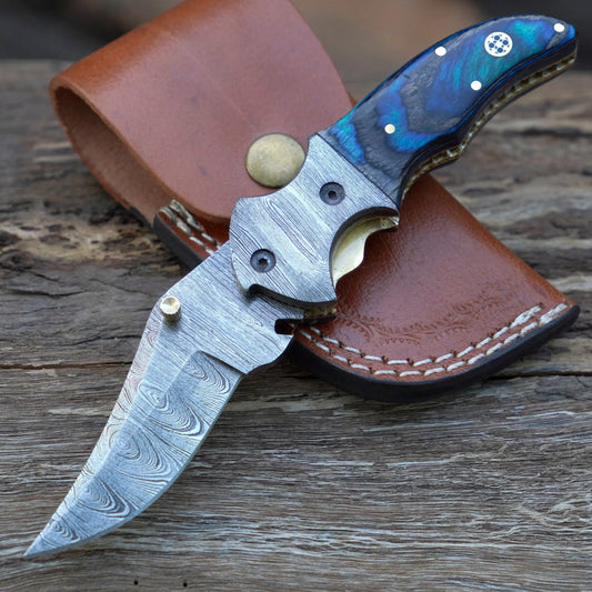 Damascus Pocket knife with a pocket clip & blue satined wood handle placed on a leather sheath